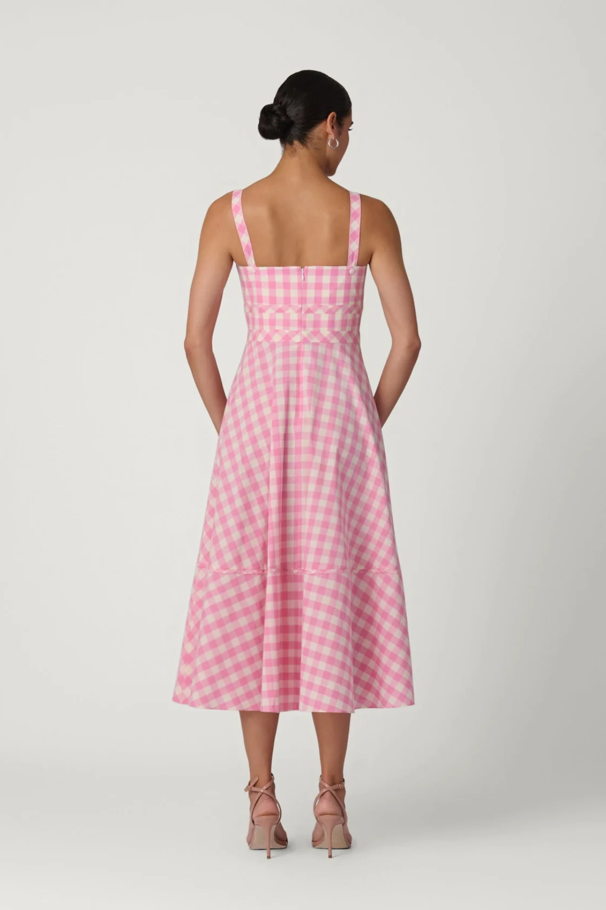 back of woman in pink gingham dress on white background 