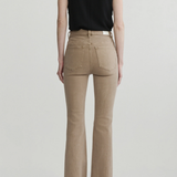 A model shown from the back wearing beige flared jeans, a black sleeveless top, and black heels against a light gray studio background.