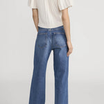 Person wearing a white top and blue jeans on a plain background