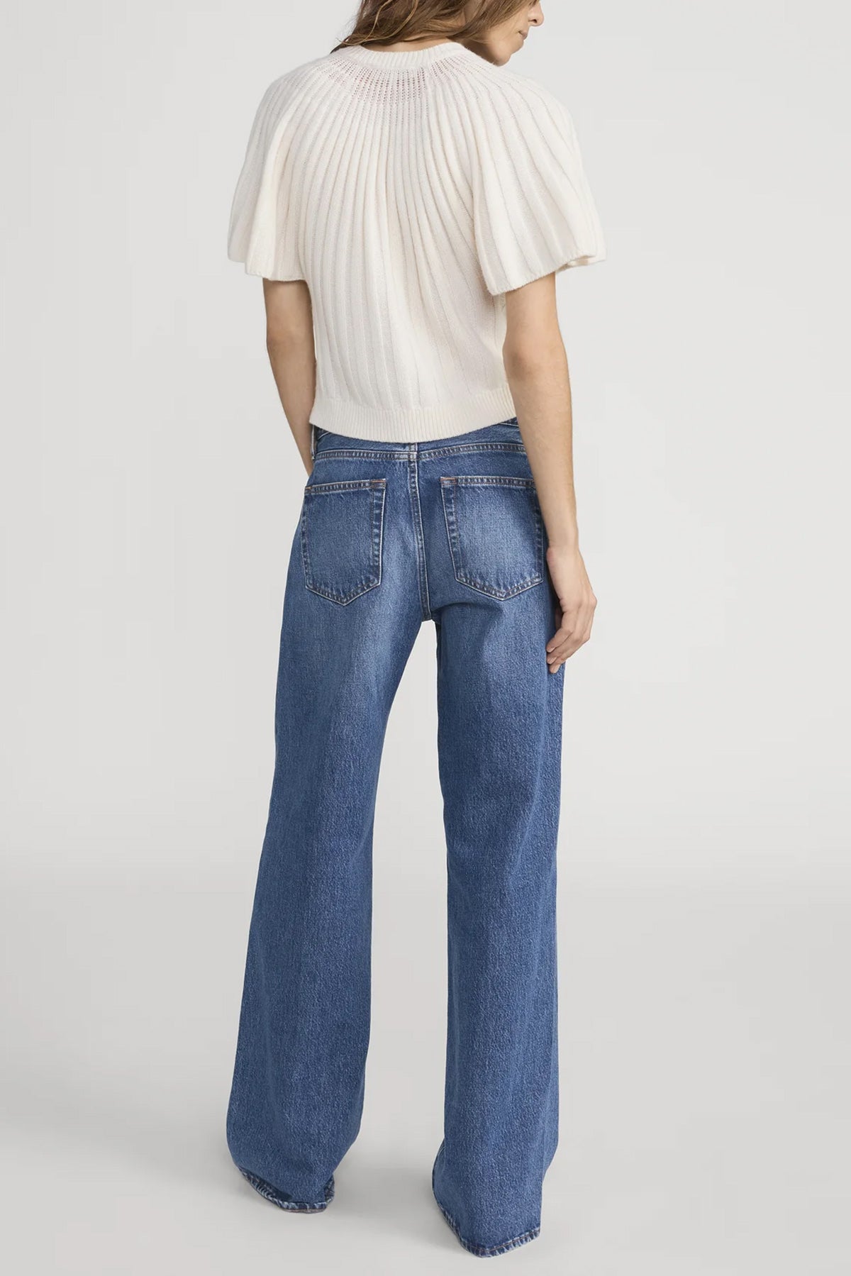 Person wearing a white top and blue jeans on a plain background