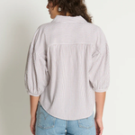 Woman wearing a light-colored striped shirt and blue jeans against a plain background