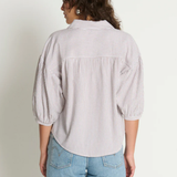 Woman wearing a light-colored striped shirt and blue jeans against a plain background