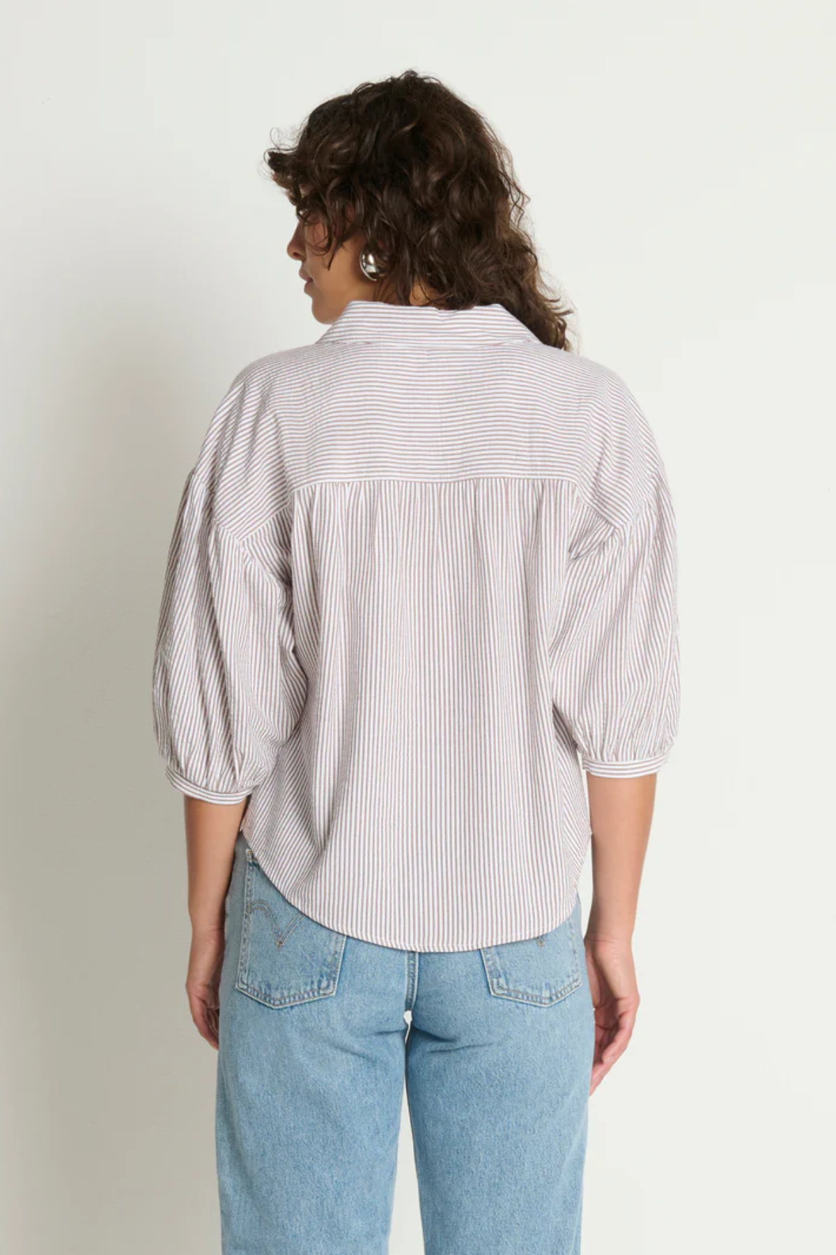 Woman wearing a light-colored striped shirt and blue jeans against a plain background
