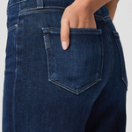 Close-up of dark blue jeans with a hand in the pocket against a neutral background