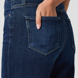 Close-up of dark blue jeans with a hand in the pocket against a neutral background