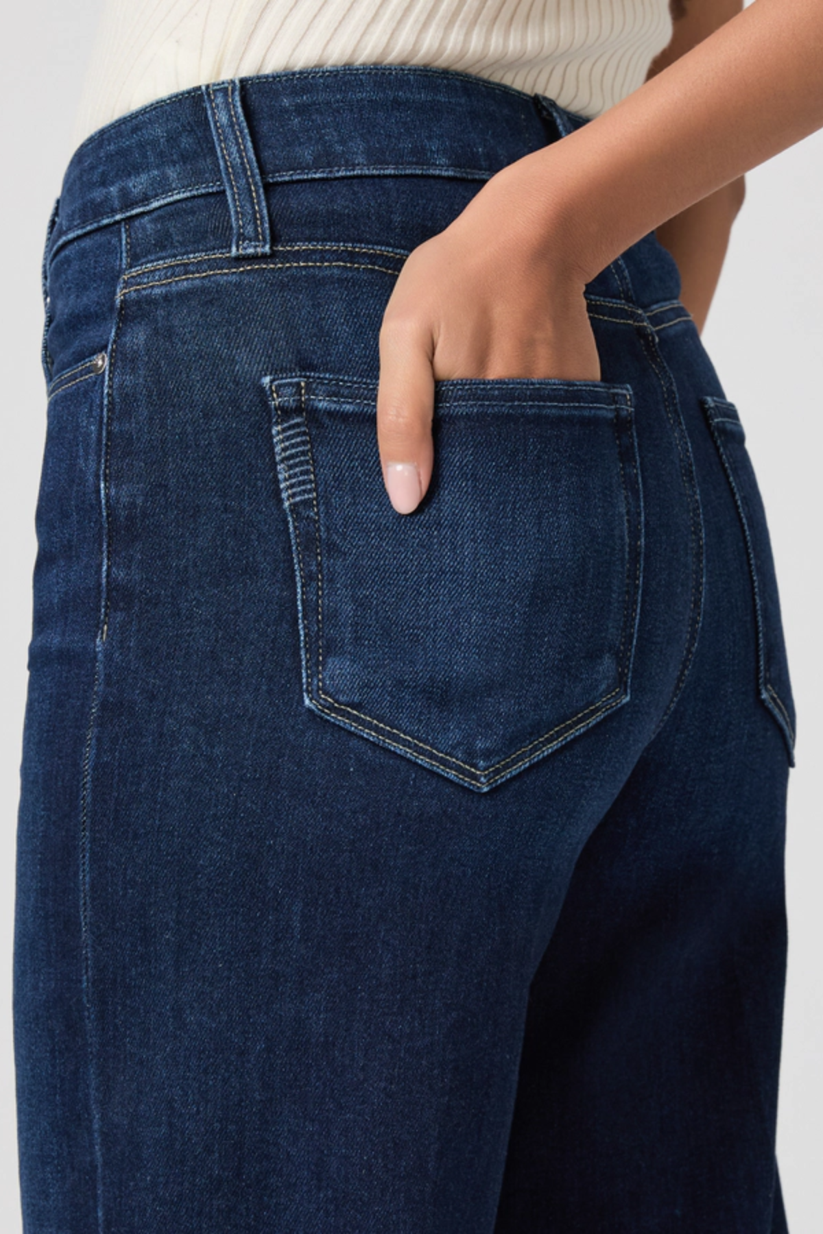 Close-up of dark blue jeans with a hand in the pocket against a neutral background