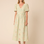 Woman wearing a light green dress with floral embroidery on a beige background