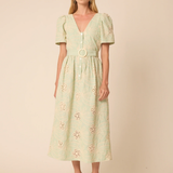 Woman wearing a light green dress with floral embroidery on a beige background