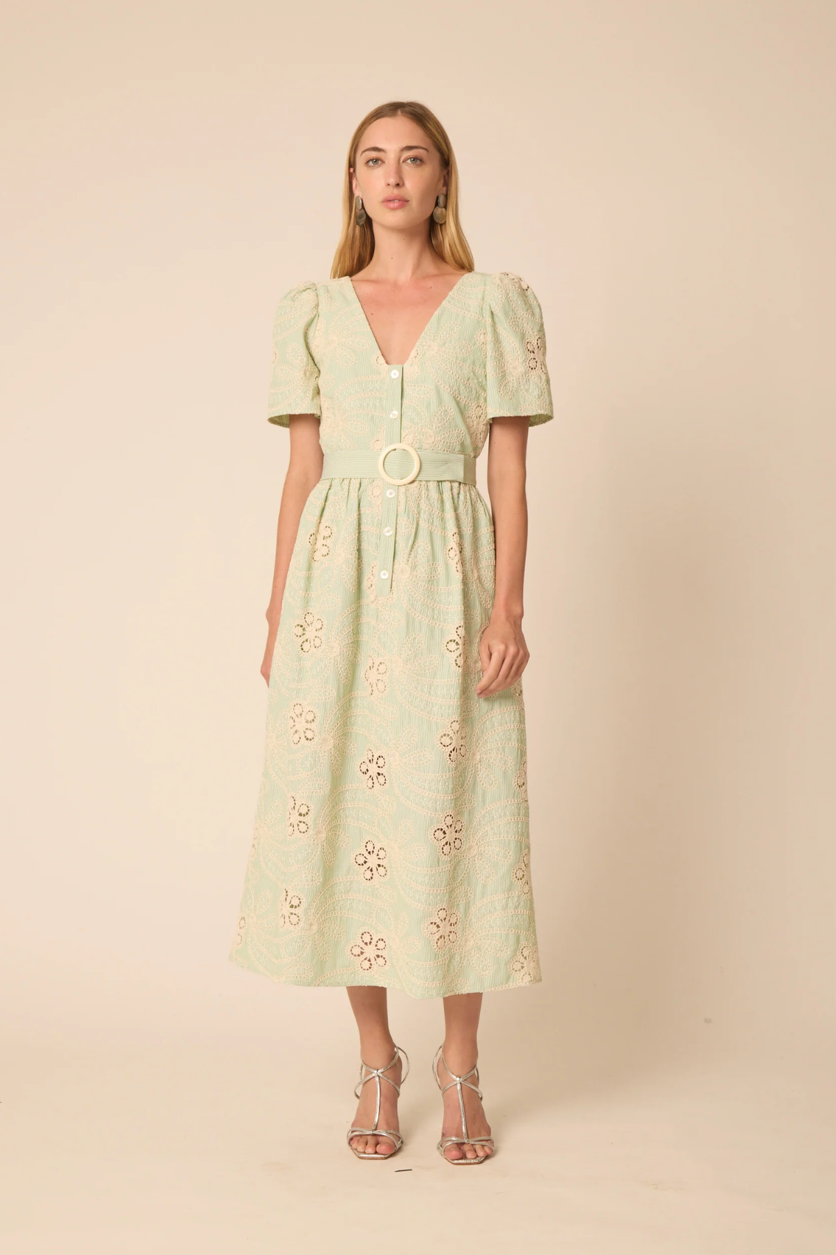 Woman wearing a light green dress with floral embroidery on a beige background