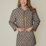 A woman modeling a long-sleeve mini dress with a brown, beige, and white geometric pattern, standing against a solid beige background.