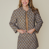 A woman modeling a long-sleeve mini dress with a brown, beige, and white geometric pattern, standing against a solid beige background.