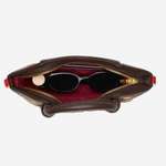 An overhead view of a brown leather handbag with its zipper open, showing a red interior lining and black sunglasses resting inside, set against a plain light gray background.