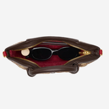 An overhead view of a brown leather handbag with its zipper open, showing a red interior lining and black sunglasses resting inside, set against a plain light gray background.