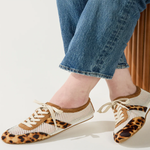 Person wearing leopard print shoes with white laces on a plain background