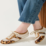 Person wearing leopard print shoes with white laces on a plain background
