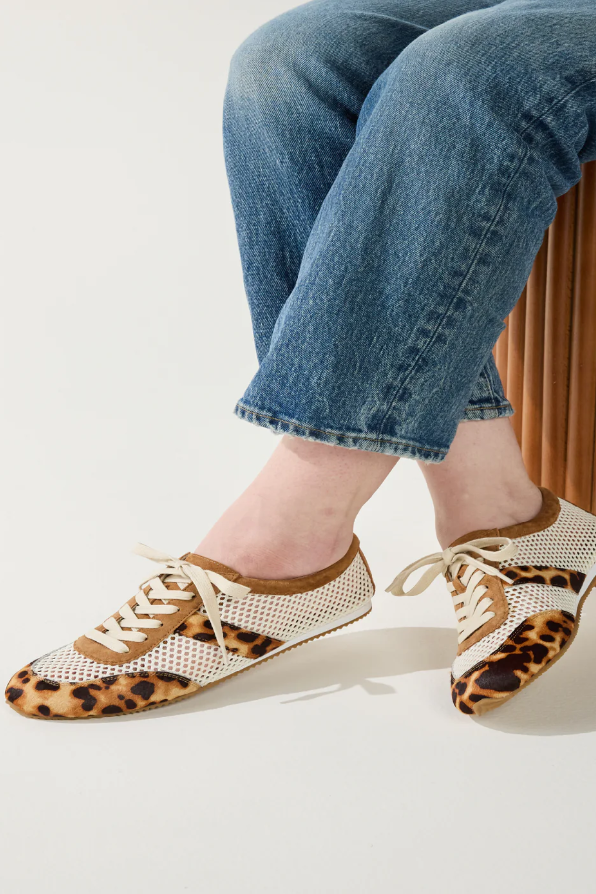Person wearing leopard print shoes with white laces on a plain background
