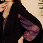 Woman wearing a black coat with purple sleeves against a beige background