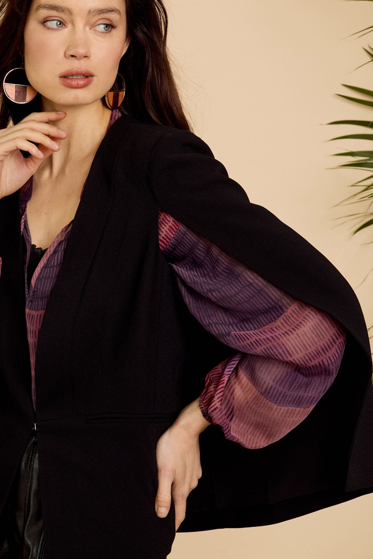 Woman wearing a black coat with purple sleeves against a beige background