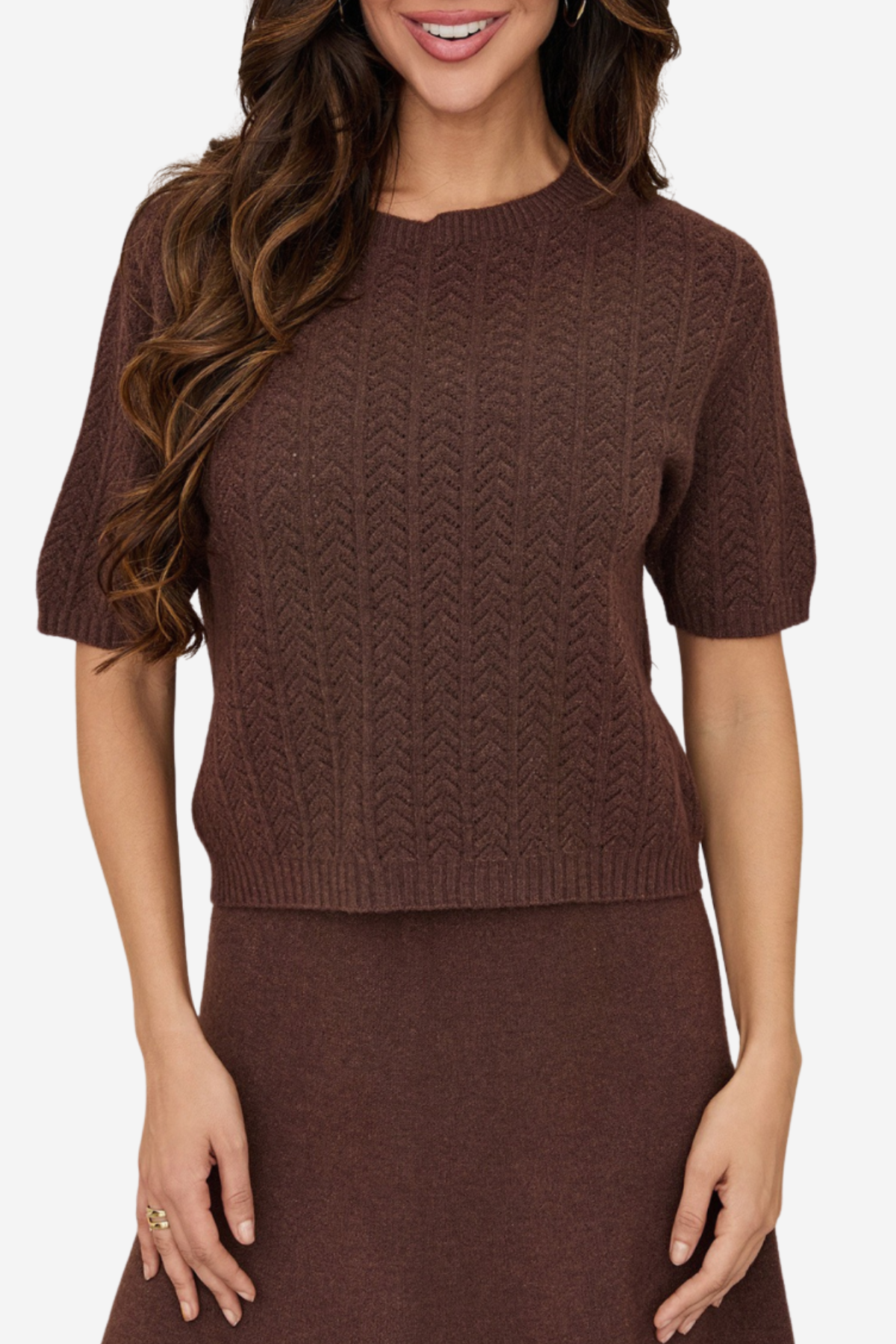 A woman wearing a brown short-sleeve knit sweater with a textured chevron pattern, paired with a matching brown skirt, against a plain light background.