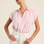 Woman wearing a pink striped shirt and white pants against a beige background