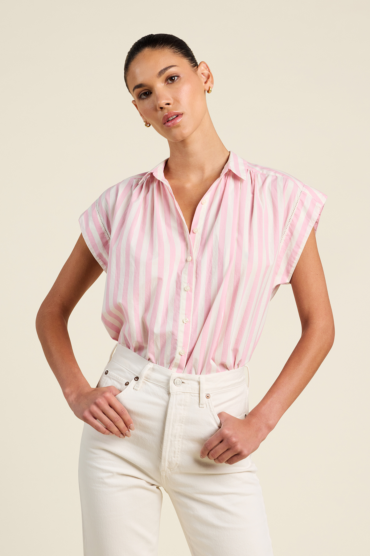 Woman wearing a pink striped shirt and white pants against a beige background
