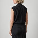 A woman shown from the back wearing a sleeveless black ribbed knit mock-neck top and a matching long black ribbed skirt against a light gray studio background.