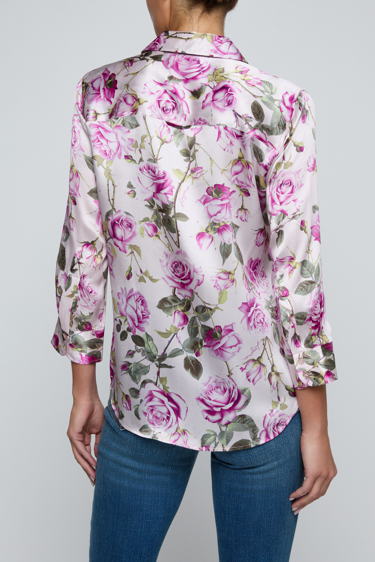 Model wearing rose print blouse with jeans on white background.