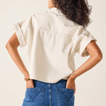 Person wearing a beige shirt and blue jeans against a plain background