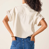Person wearing a beige shirt and blue jeans against a plain background