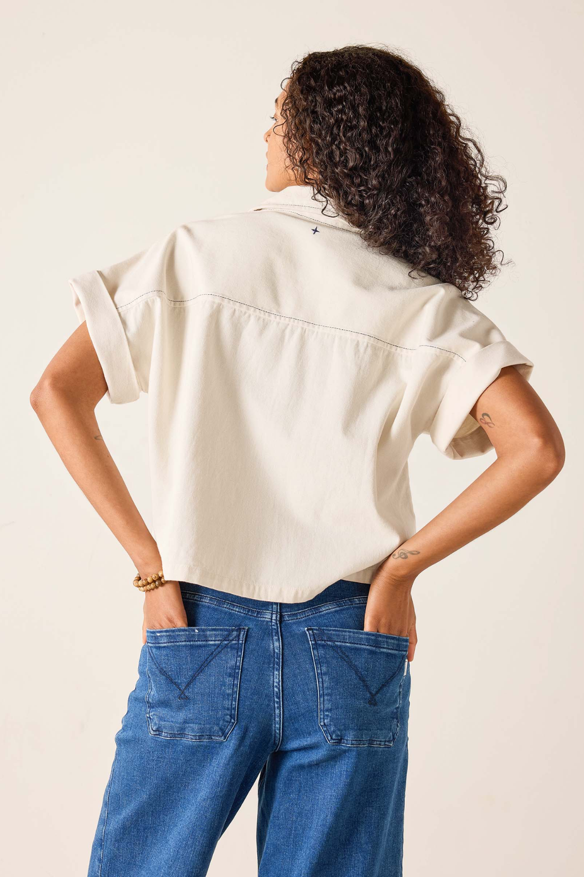 Person wearing a beige shirt and blue jeans against a plain background