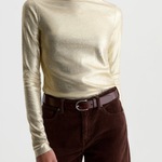 A woman wearing a metallic champagne-gold long-sleeve mock neck top and dark brown corduroy pants with a brown leather belt, photographed against a light gray studio background.