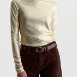 A woman wearing a metallic champagne-gold long-sleeve mock neck top and dark brown corduroy pants with a brown leather belt, photographed against a light gray studio background.