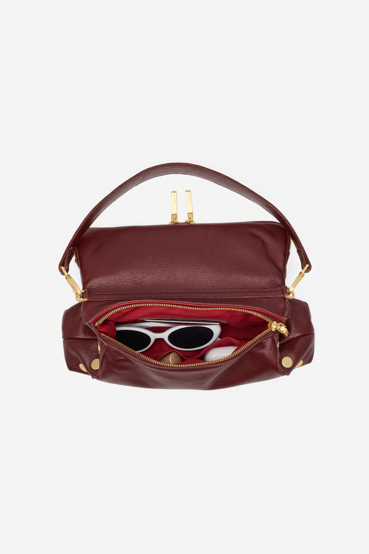 A burgundy leather handbag with gold-tone hardware, shown open to reveal a red interior lining and white sunglasses inside, set against a plain light gray background.