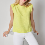 Woman wearing a yellow sleeveless top and white pants against a plain background
