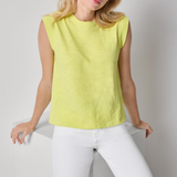 Woman wearing a yellow sleeveless top and white pants against a plain background