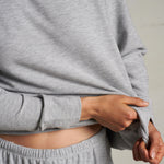Woman wearing a light grey long-sleeve knit top with a relaxed fit, photographed against a soft neutral backdrop.