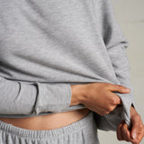 Woman wearing a light grey long-sleeve knit top with a relaxed fit, photographed against a soft neutral backdrop.