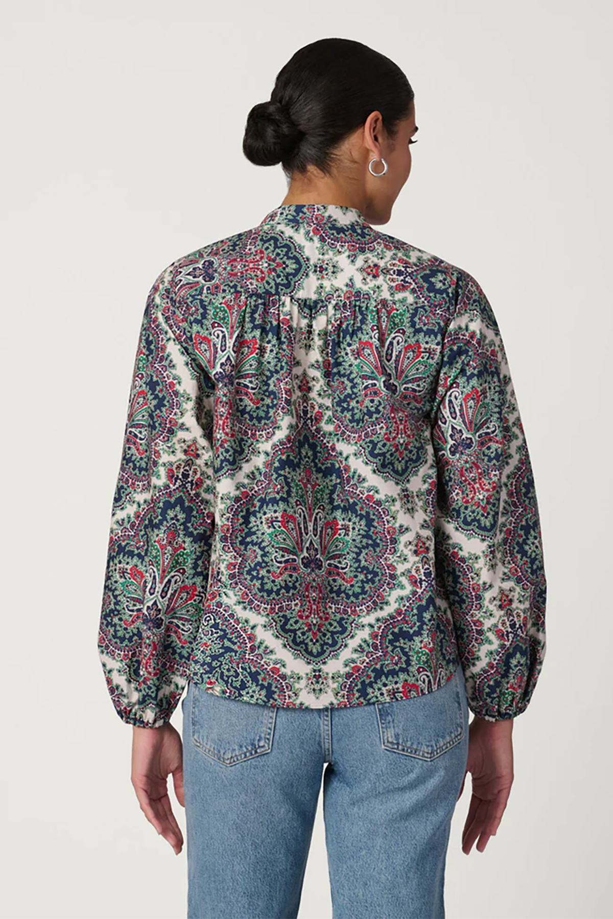 Person wearing a patterned shirt and jeans on a plain background