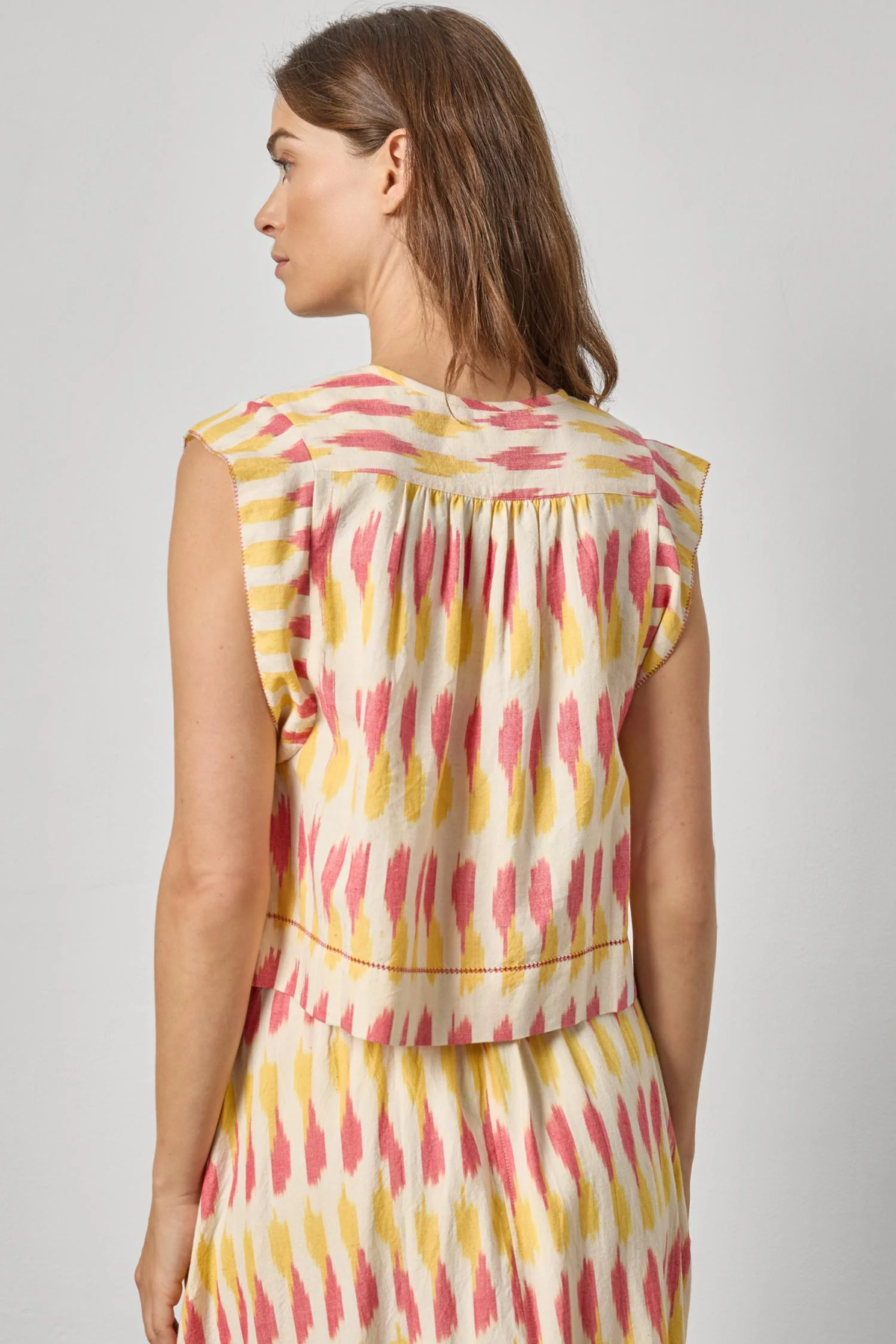 Woman wearing a sleeveless dress with a colorful abstract pattern on a plain background