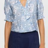 Woman wearing a blue floral blouse and navy shorts on a white background