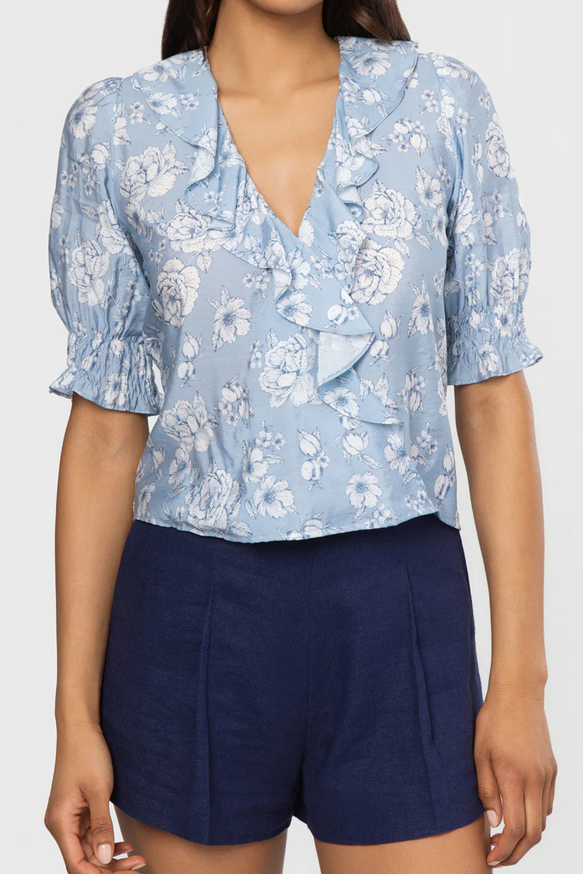 Woman wearing a blue floral blouse and navy shorts on a white background