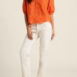 woman in orange eyelet top and white denim on tan background 