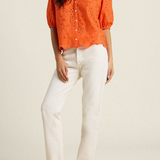 woman in orange eyelet top and white denim on tan background 