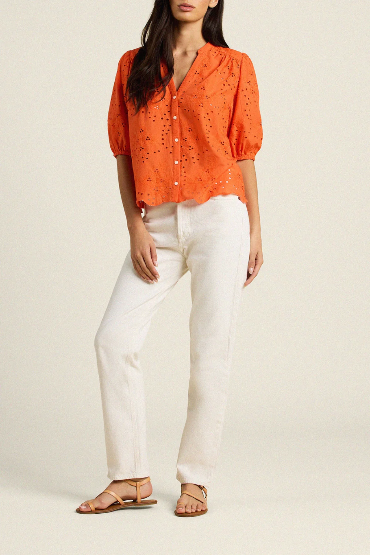 woman in orange eyelet top and white denim on tan background 