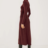 Woman wearing a long burgundy dress with black boots on a white background