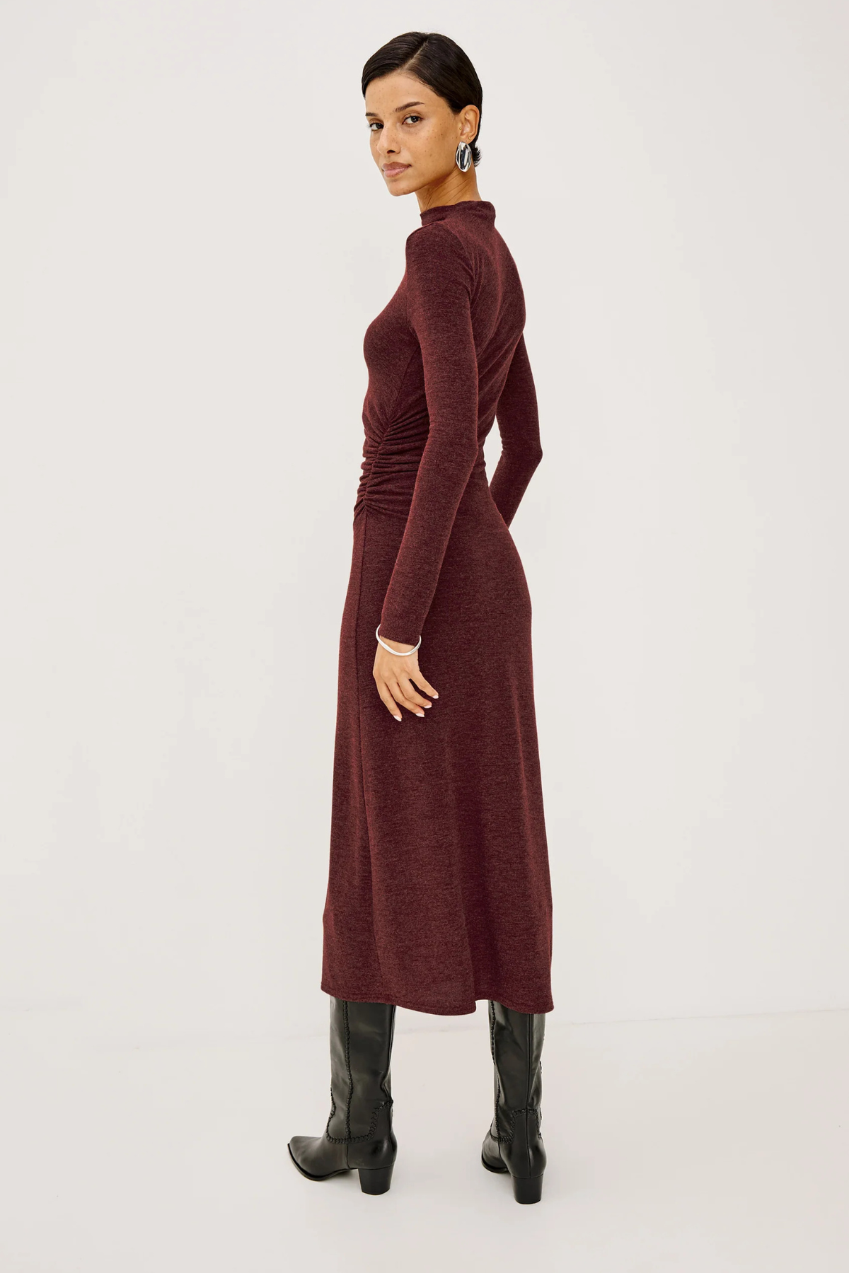 Woman wearing a long burgundy dress with black boots on a white background