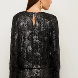 A woman shown from the back wearing a black long-sleeve sequined dress with fringe detailing and a small keyhole cutout at the neckline, against a plain light background.