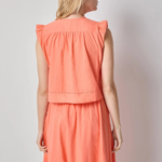 Woman wearing a coral sleeveless top and skirt set against a plain background