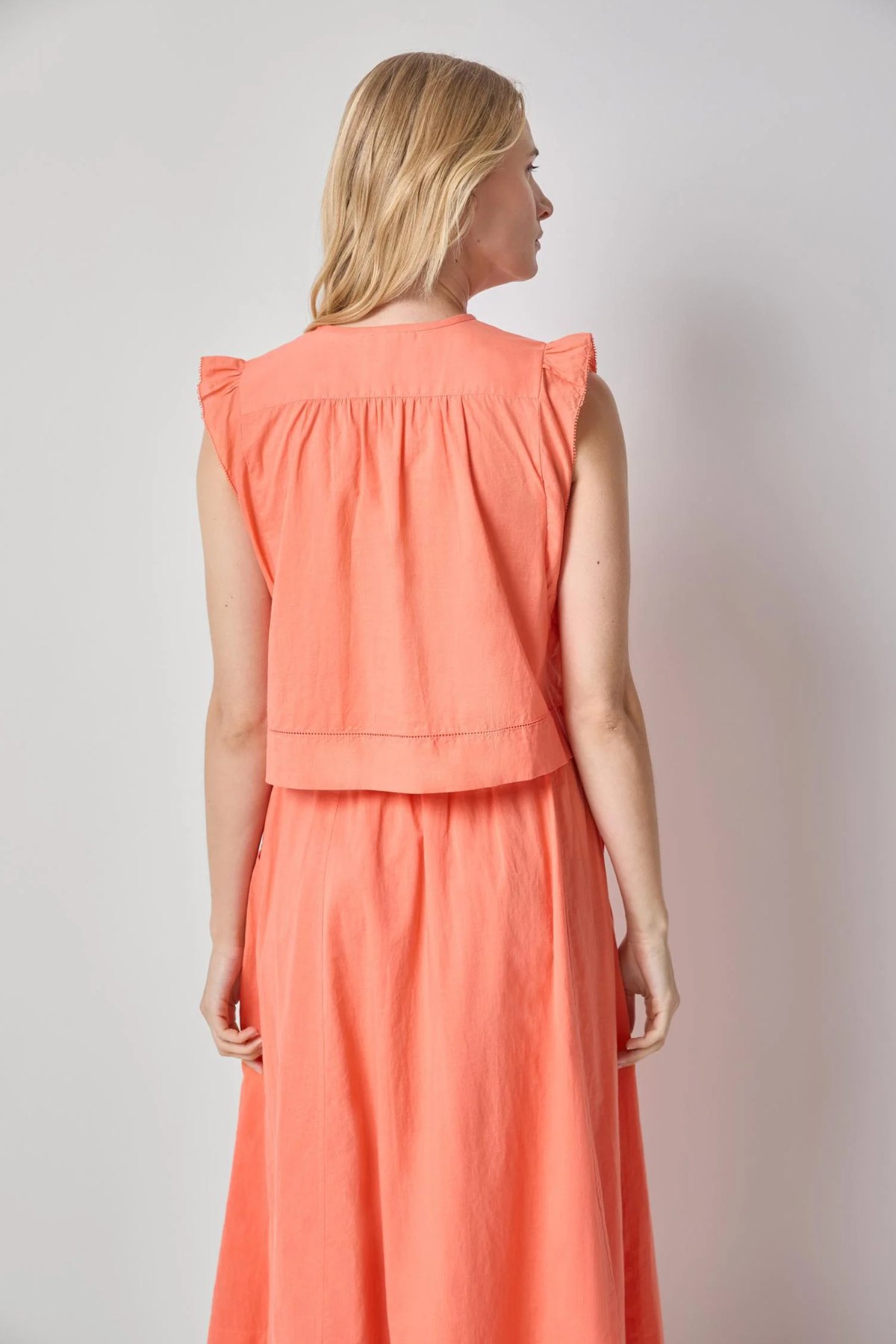 Woman wearing a coral sleeveless top and skirt set against a plain background