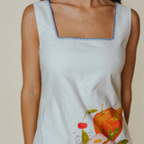 Woman wearing a sleeveless dress with a floral and fruit design on a plain background